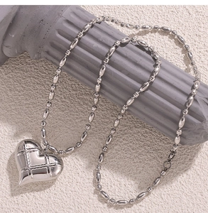 Close-up of hollow heart pendant with quilted texture on silver bead chain on stone