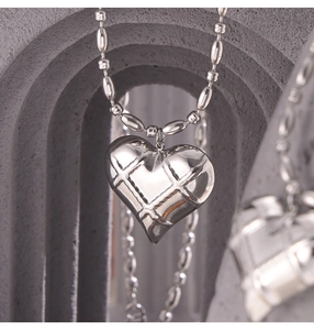 Macro shot of silver heart pendant with quilted texture on oval bead chain