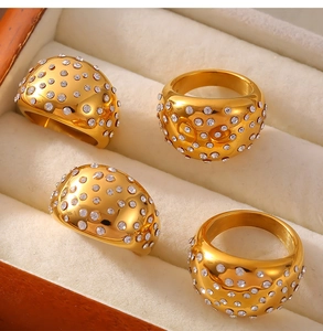Close-up of four wide gold-finished rings with crystal pave settings in a jewelry box