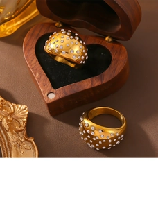 Close-up of wide gold-plated band rings with pavé cubic zirconia in a wooden heart box