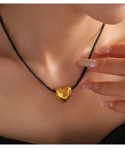 Detailansicht einer schwarzen Kordelkette mit glänzendem goldenem Herzanhänger am Model