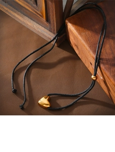 Detail eines polierten goldenen Herzanhängers an einer schwarzen Kordel mit Goldperle