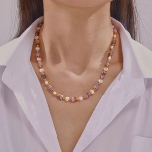 Collier vintage avec cristaux violets, perles et billes dorées sur une chemise blanche