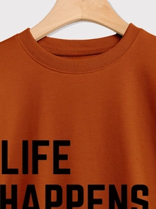 Detail of the crew neck collar and Life Happens print on a burnt orange sweatshirt