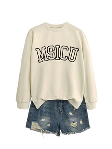 Flat lay of cream oversized MSICU sweatshirt paired with distressed denim shorts