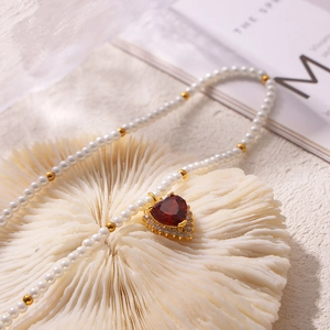 Elegant pearl necklace with red heart zircon pendant and gold accents on coral stand
