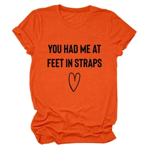 Detail eines orangenen Kurzarm-T-Shirts mit 'YOU HAD ME AT FEET' Druck und Herzmotiv