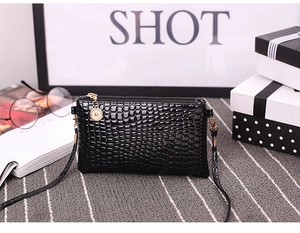 Detail of crocodile embossed black crossbody bag with gold zipper on fashion magazine