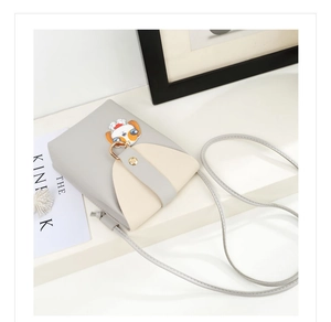 Close-up of mini cartoon crossbody bag with dog charm and gray-white patchwork leather