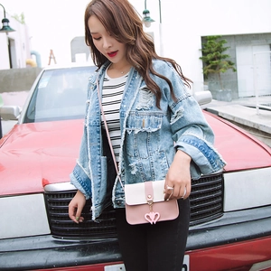 Outdoor street style shot of a pink and beige crossbody bag with heart pendant detail