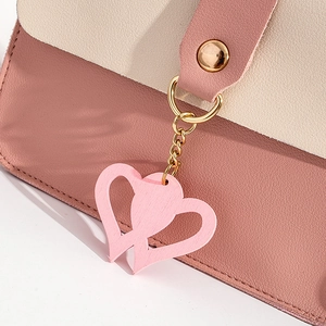 Close-up of pink pebbled leather bag with gold heart pendant and magnetic snap buckle