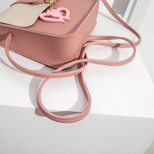 Close-up of pink and beige crossbody bag with pebbled leather texture and heart charms
