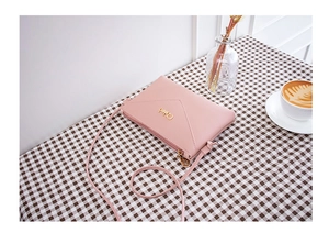 Pink PU leather envelope crossbody bag with gold logo on a rustic checkered tablecloth