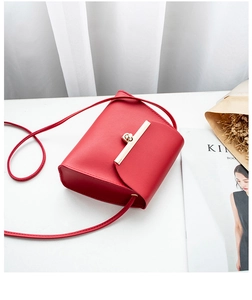 Detail of red minimalist crossbody bag featuring a sleek golden metal clasp on a desk