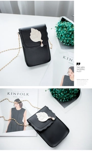 Détail du mini sac à téléphone noir avec rabat ondulé et charm perle sur table blanche