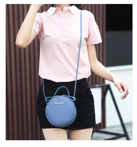 Blue round mini crossbody bag with bow detail and top handle shown on a model