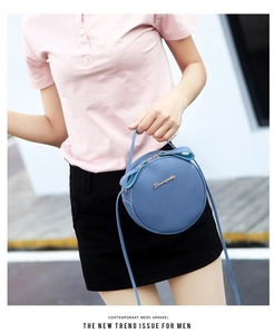 Detail of blue circular mini crossbody bag with litchi grain texture and gold logo