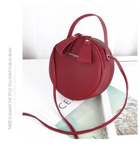 Detail of red round leather crossbody bag with dual zippers and pebble texture surface