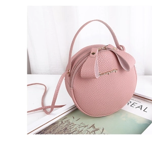 Pink round leather handbag detail with pebble texture and gold logo on white fabric