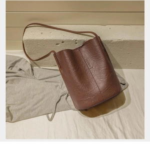Detailed view of brown textured leather bucket bag with XOVINO brand label on stone