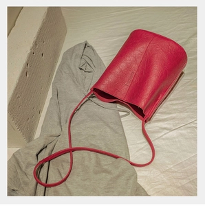 Detail view of the embossed XOVINO brand logo on a rose red pleated bucket bag