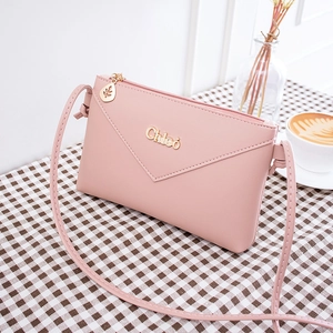Pink envelope crossbody phone bag with gold leaf charm and Chleo logo on plaid background