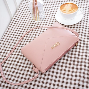 Pink leather crossbody phone bag with gold logo on a plaid tablecloth setting