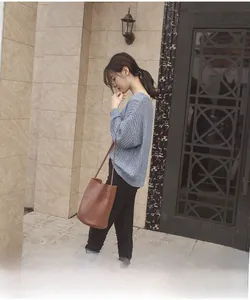 Street style view of a brown leather bucket bag paired with a light blue knit sweater