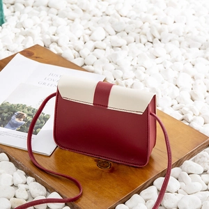 Mini crossbody bag with burgundy and cream contrast colors on a textured wooden base