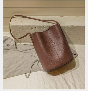 Close-up of a dark brown bucket bag featuring pleated leather texture and branded label