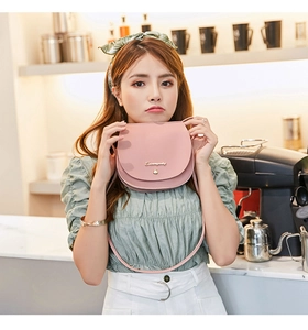 Pink saddle bag with gold logo and round buckle detail in a cozy cafe setting