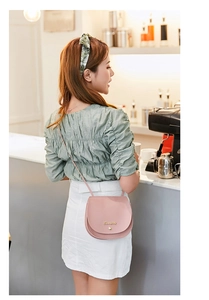 Close-up of pink saddle bag with golden logo lettering held by a model in a cafe