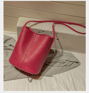 Close-up of dark red bucket bag with pleated leather texture and embossed logo