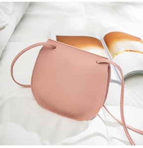 Detailed view of a soft pink saddle bag in matte leather on a white quilted background