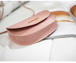 Detail of pink matte leather saddle bag featuring a gold metal trim and flap closure