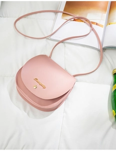 Pink saddle crossbody bag in faux leather on quilted bedding with fashion magazines