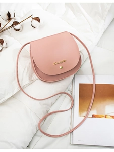 Pink PU leather saddle bag with gold metal logo on soft white bedding background