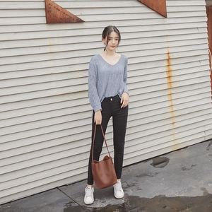 Woman in blue knit sweater and black jeans holding a large brown leather bucket bag