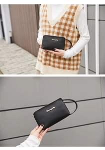 Detail of black pebbled leather wristlet with golden metal logo and zip closure
