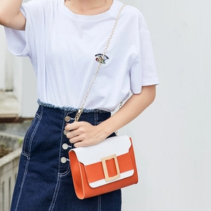 Sac bandoulière bicolore avec grande boucle dorée et chaîne présenté par un mannequin
