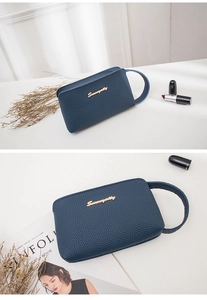 Macro detail of dark blue litchi grain leather clutch bag with golden metal logo