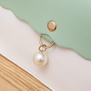 Elegant mint green and white crossbody bag with wave flap and pearl charm on wood