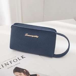 Navy blue lychee grain leather wristlet clutch bag with gold logo on white stand