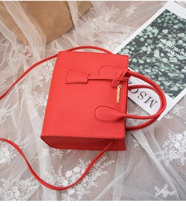 Dettaglio borsa rossa con trama litchi e logo dorato su pizzo bianco e sfondo rivista