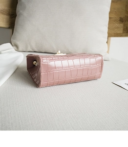 Détail du sac à main rose gaufré crocodile avec fermoir en métal doré sur canapé