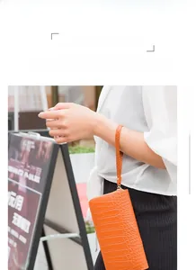 Detail of bright orange crocodile embossed wristlet wallet with metal zipper and strap
