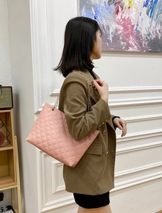 Detalle de un bolso shopper rosa acolchado con cadena dorada usado por modelo