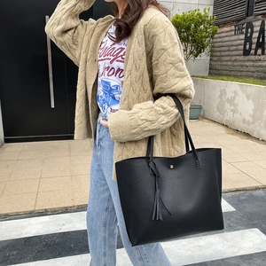 Large black litchi texture tote bag with tassel detail worn with a beige cardigan