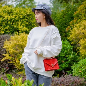 White oversized hoodie paired with a red crocodile pattern chain bag in a garden setting