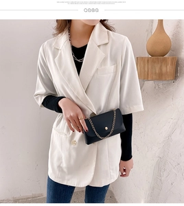 Fashionable black mini flap bag with gold chain strap shown on a white blazer outfit